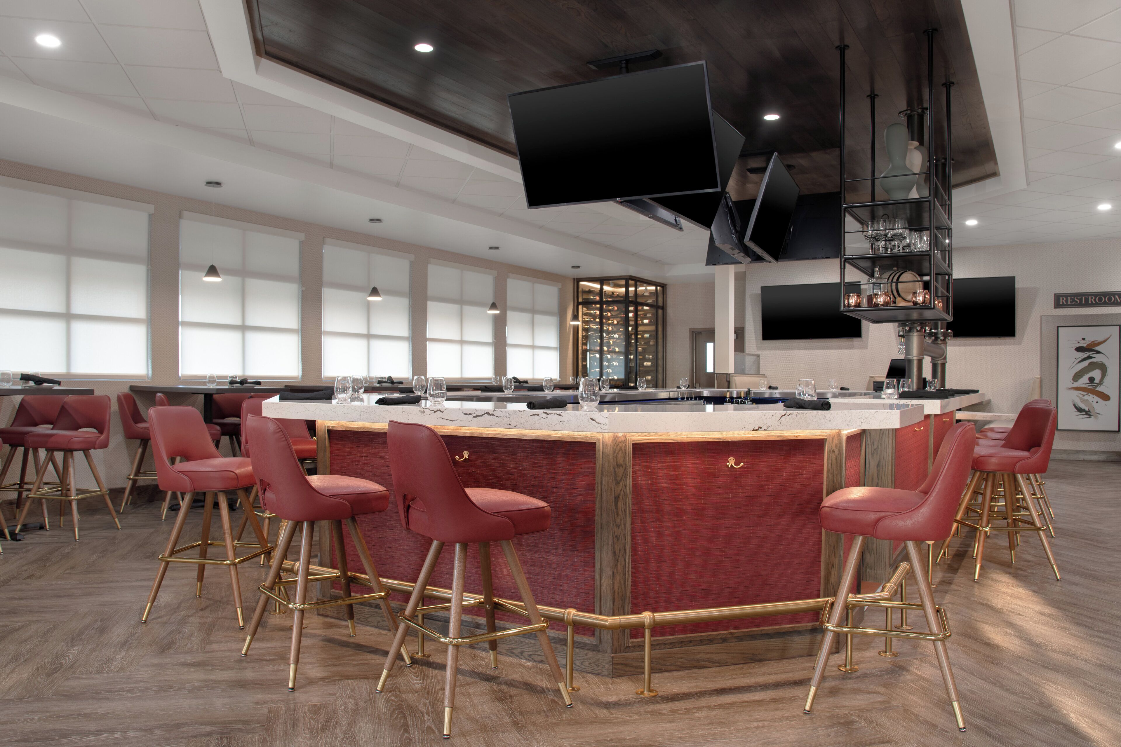 A modern bar area with a marble countertop, red upholstered bar stools, and a wine rack.