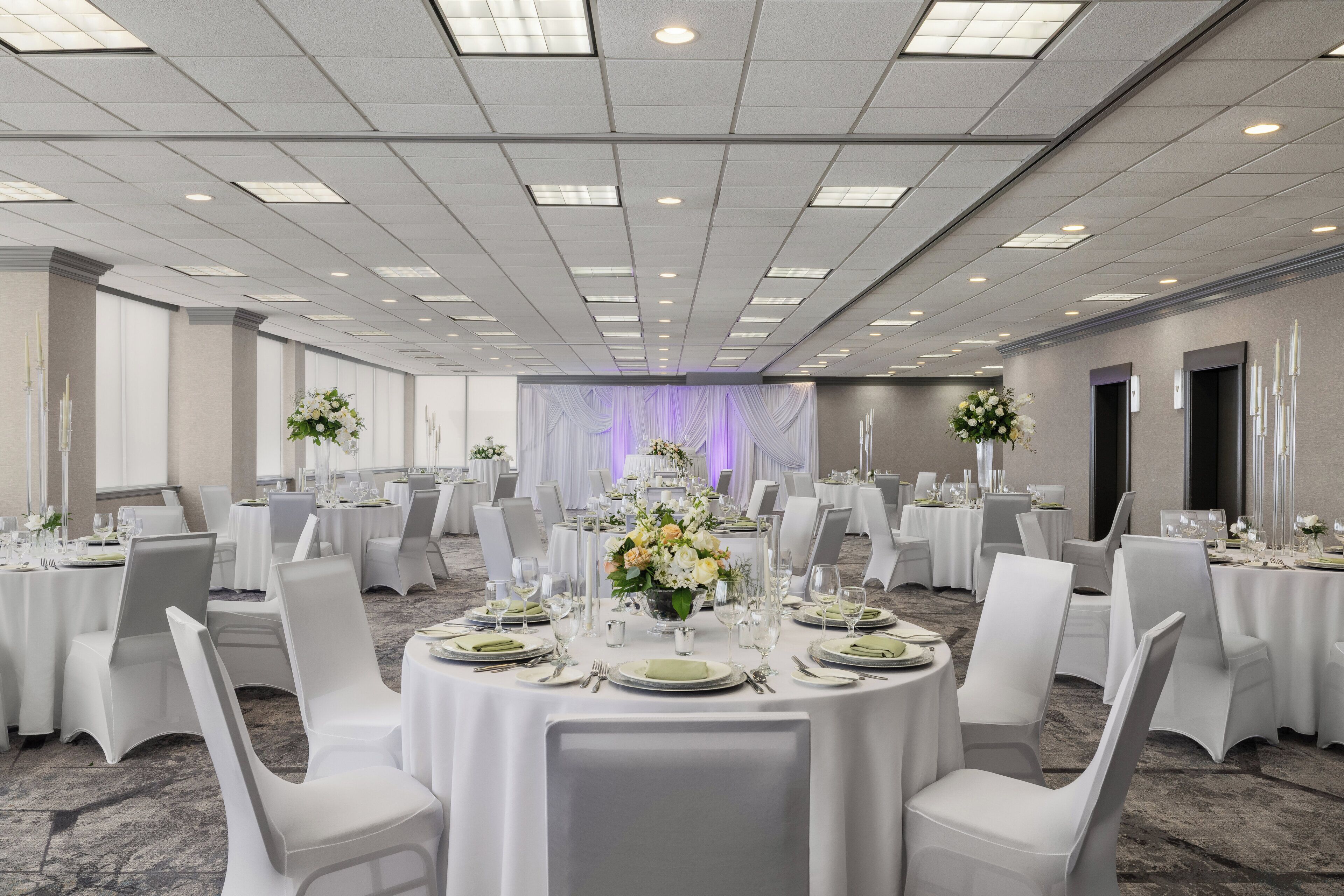A banquet hall with round tables, white chairs, and floral centerpieces.