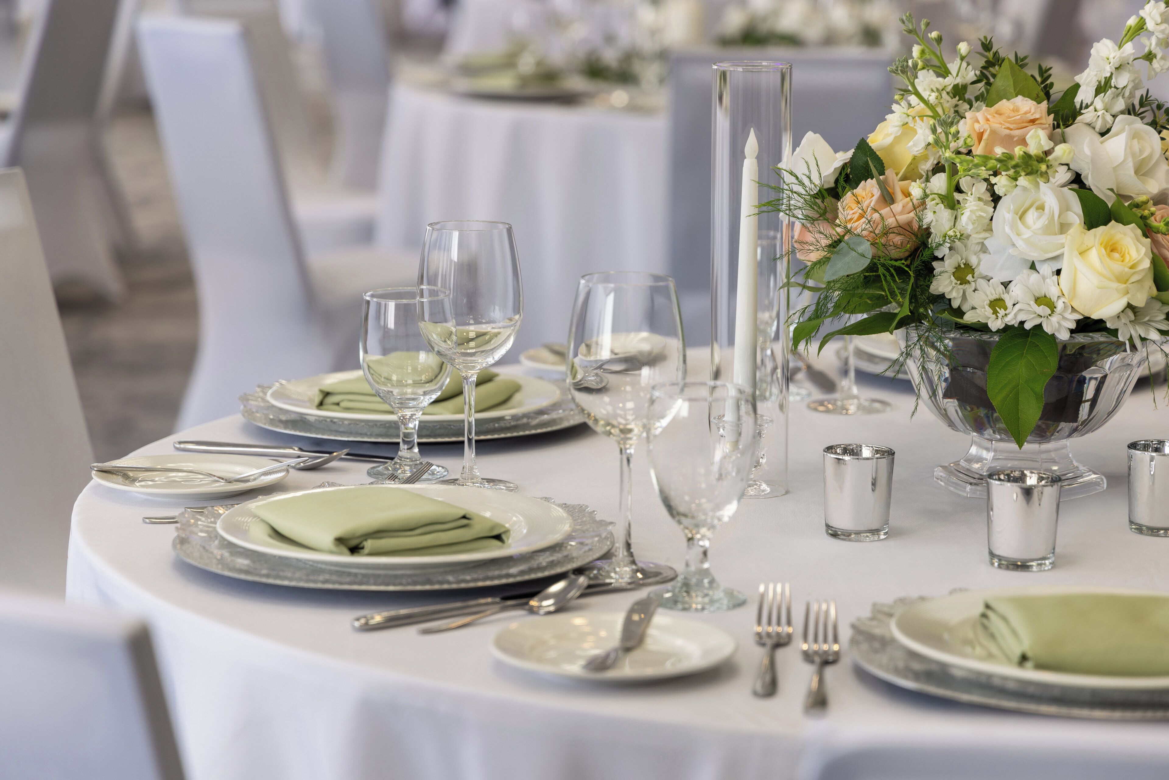 Une table dressée pour un événement formel, avec de la vaisselle transparente, des couverts en argent et un centre de table composé de fleurs.