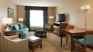 Habitación de hotel con sofá, sillón, reposapiés, televisor y mesa de comedor.