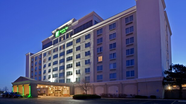 A multi-story hotel with a prominent sign, a covered entrance, and a parking lot. - Holiday Inn & Suites Overland Park West by IHG (Lenexa)