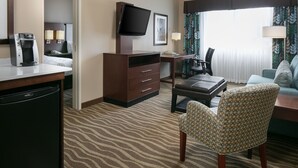 Habitación de hotel con cama, escritorio con cafetera, televisión, silla y sofá.