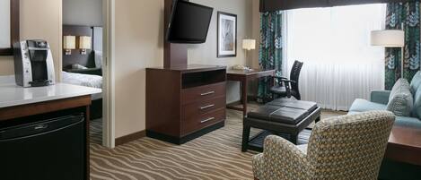 Ein Hotelzimmer mit einem Bett, einem Schreibtisch mit Kaffeemaschine, einem Fernseher, einem Sessel und einer Couch.