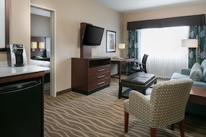 A hotel room with a bed, a desk with a coffee maker, a television, a chair, and a sofa.