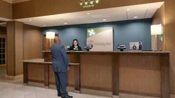 Un mostrador de recepción de hotel con un letrero que dice 'Welcome Check-in', un quiosco digital y una barra de recepción.