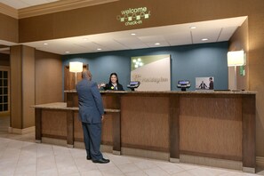A hotel reception desk with a 'Welcome Check-in' sign, a digital kiosk, and a reception counter. - Holiday Inn & Suites Overland Park West by IHG (Lenexa)
