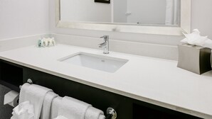 Un baño con un espejo grande, un lavamanos, un perchero para toallas y un cuadro en la pared.