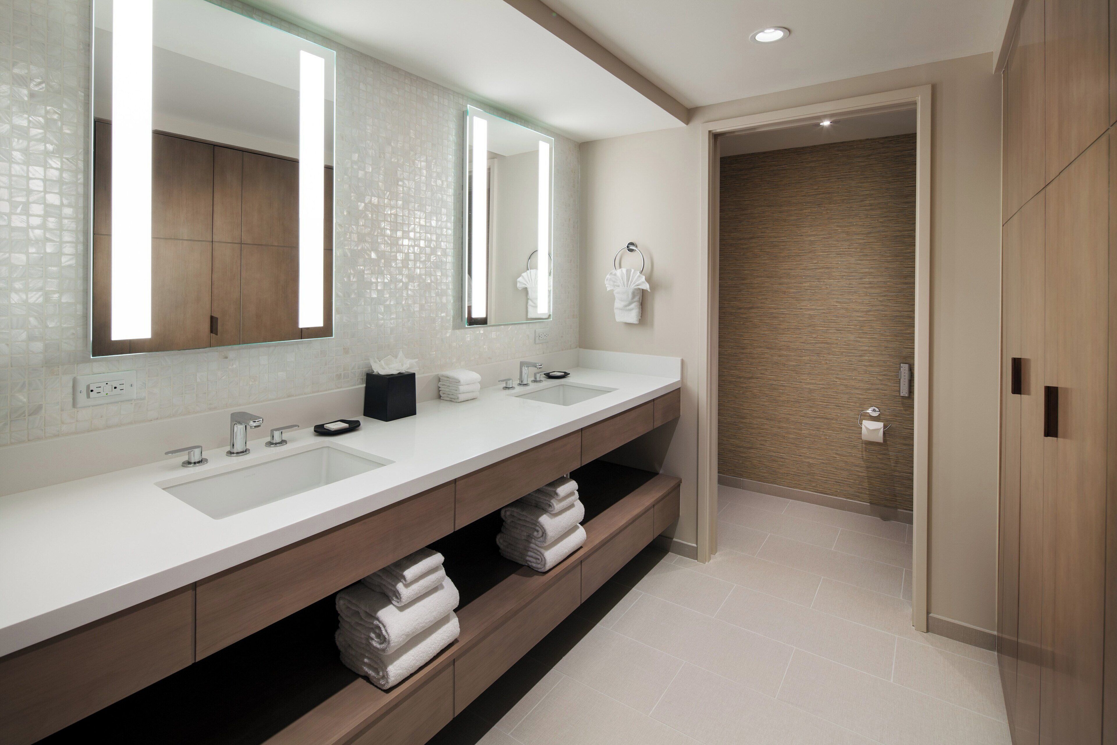 A modern bathroom with a large mirror, two sinks, and a wooden vanity.