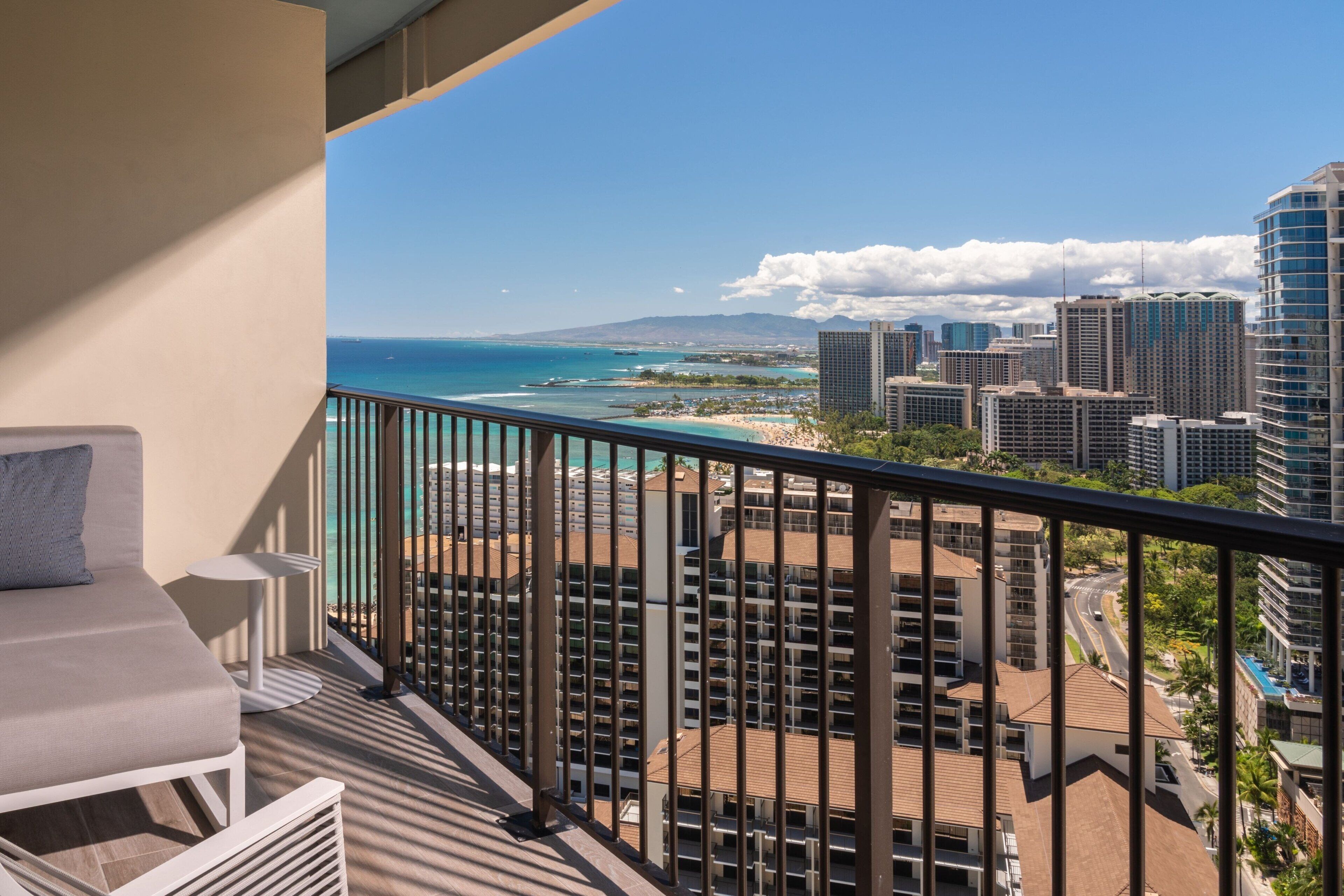 A balcony with a view of the ocean and cityscape, including high-rise buildings and a beach.