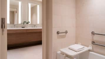A modern bathroom with a white sink, mirror, and toilet. There are grab bars near the toilet and a towel rack.