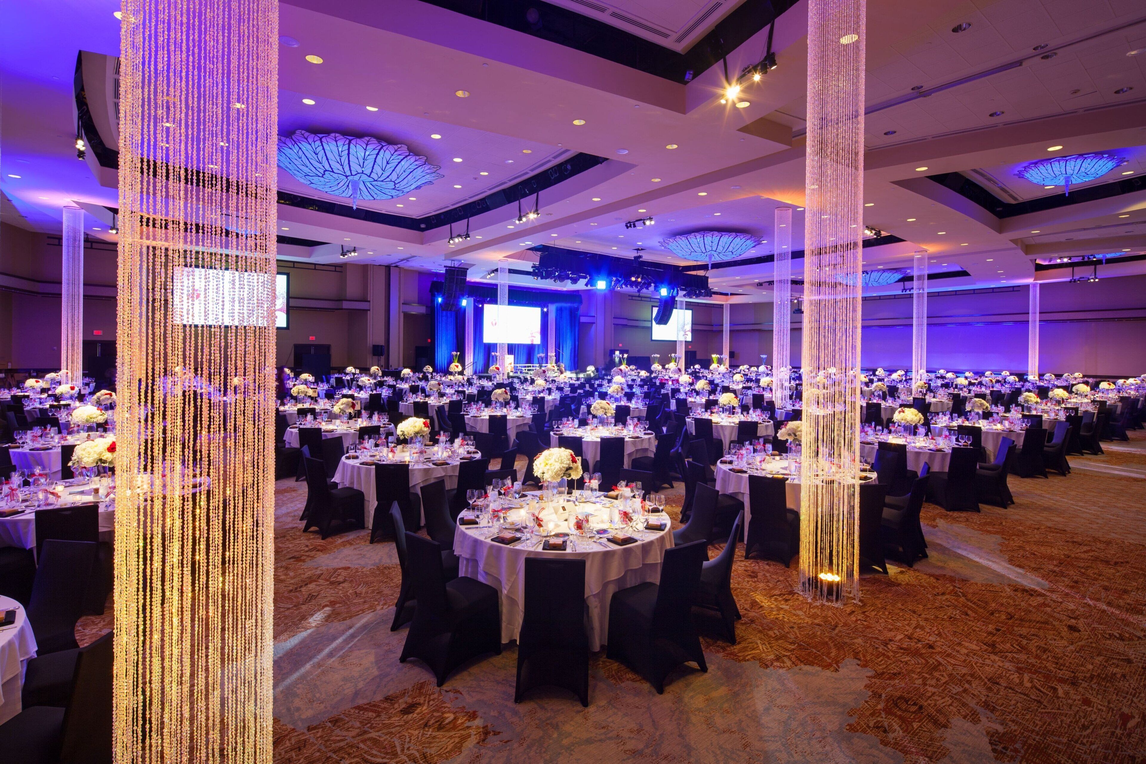 A banquet hall with round tables, black chairs, and floral centerpieces.