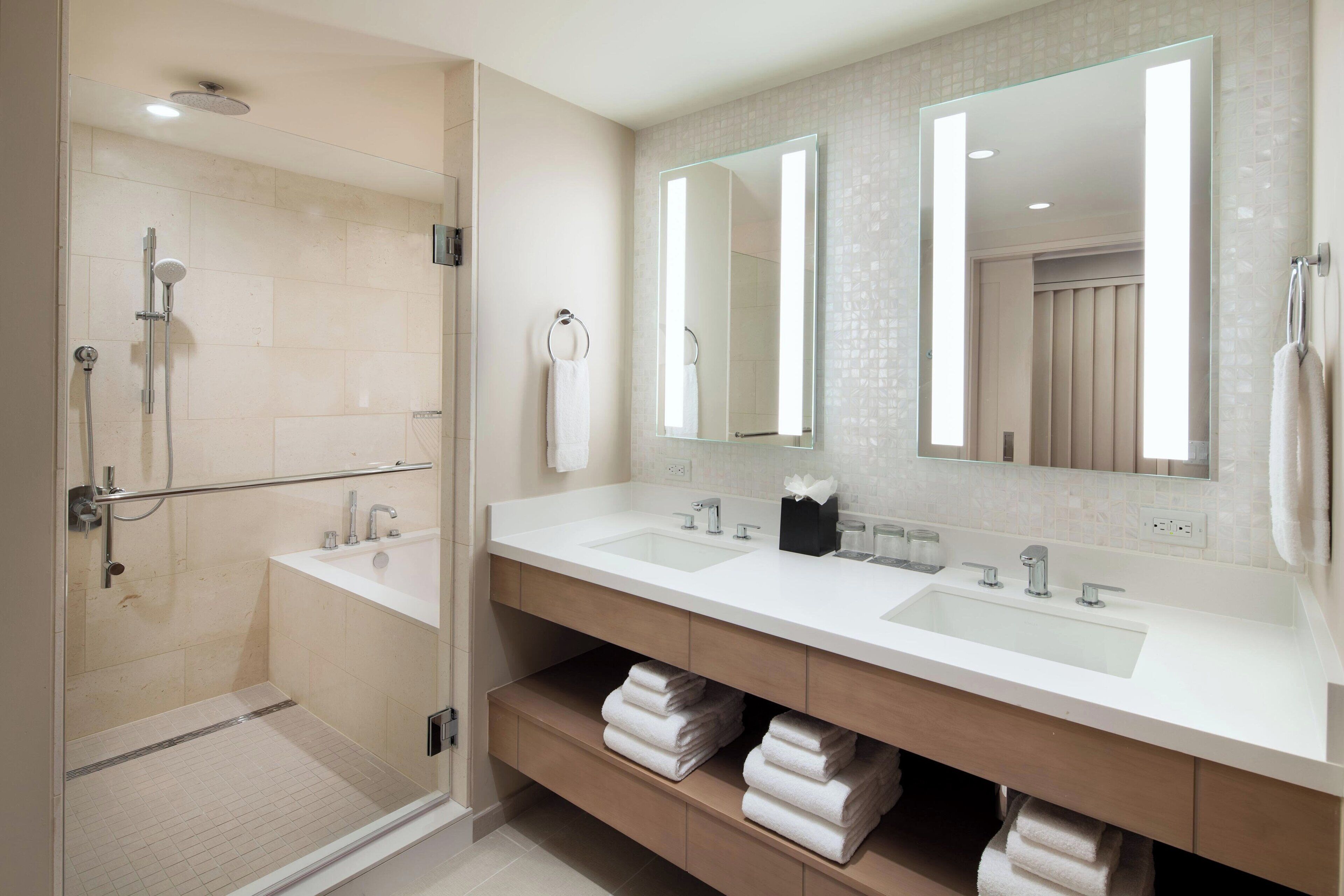 A modern bathroom with a walk-in shower, two sinks, and a large mirror.