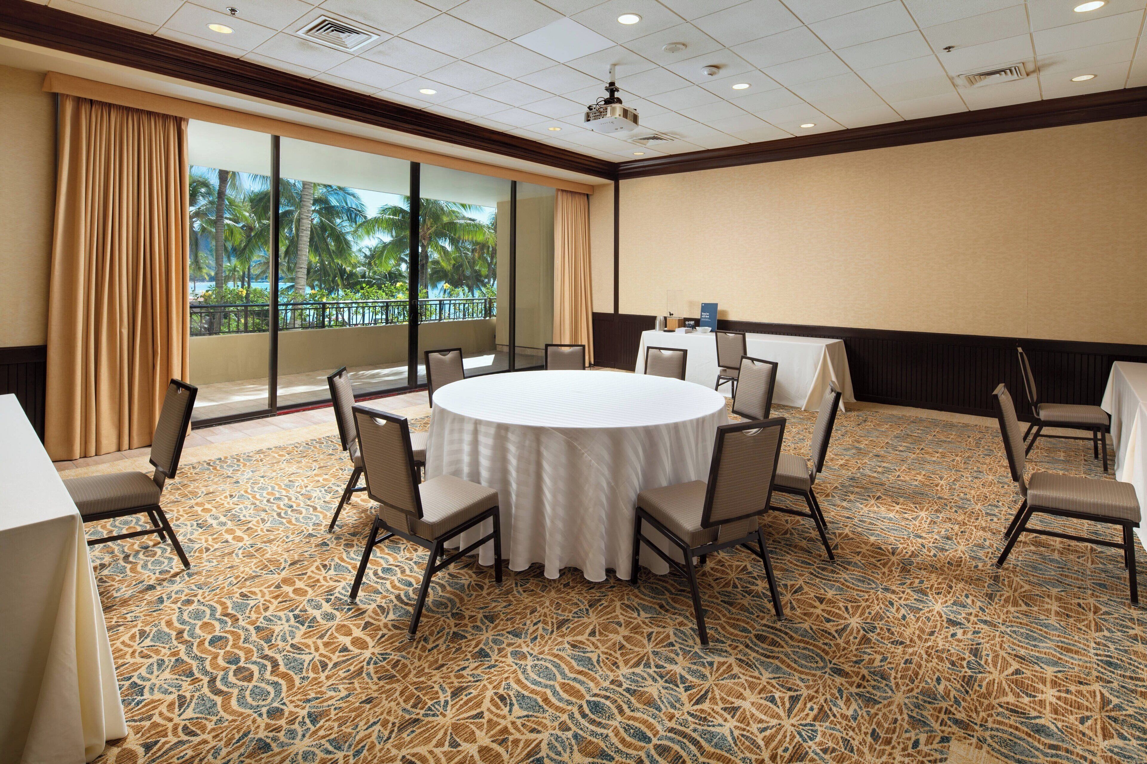 A conference room with a round table, chairs, and a large window with a view of palm trees.