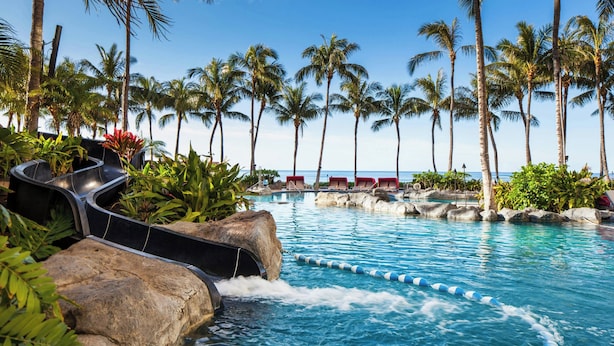 A pool area with a water slide, palm trees, and lounge chairs. - Sheraton Waikiki Beach Resort (Honolulu)
