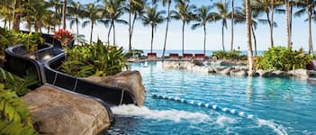 A pool area with a water slide, palm trees, and lounge chairs.
