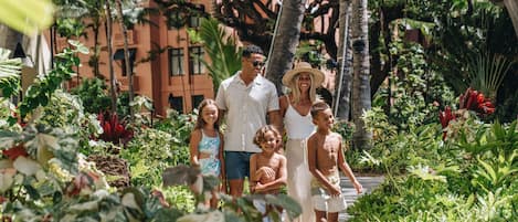 A family walking on a pathway surrounded by lush greenery and palm trees.