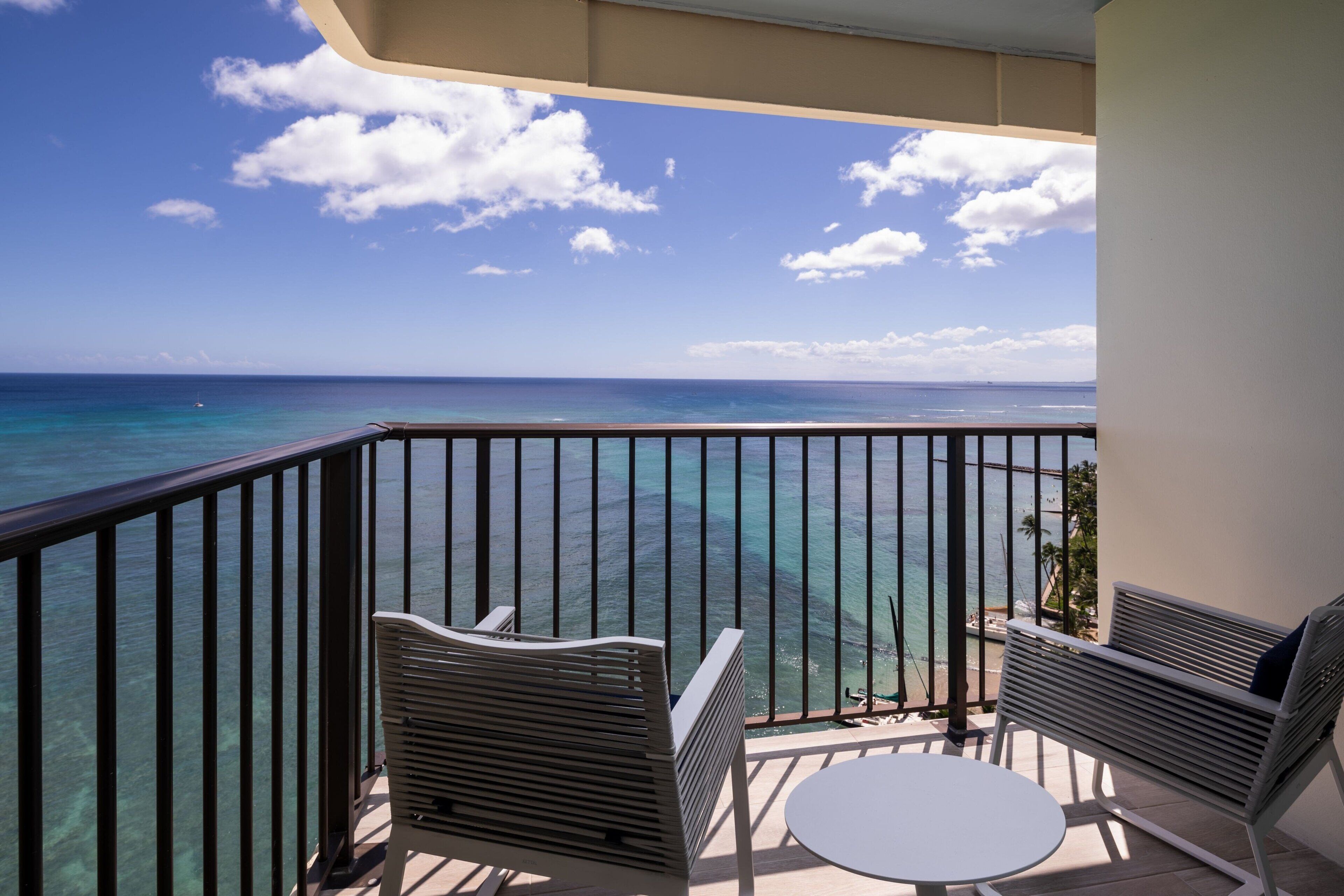 A balcony with a view of the ocean, two chairs, and a small table.