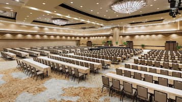 A large conference room with rows of tables and chairs, high ceilings with recessed lighting, and a patterned carpet.