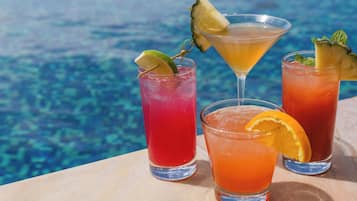 Three drinks with fruit garnishes on a table by a pool.