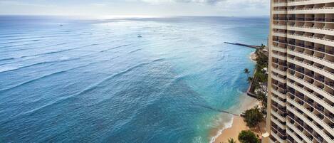 A high-rise hotel overlooking a beach with clear blue waters and a sandy shore.