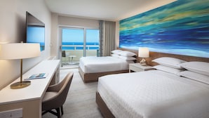 A hotel room with a large bed, a desk with a chair, a TV, and a painting of a blue ocean view. - Sheraton Waikiki Beach Resort (Honolulu)