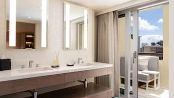 A modern bathroom with a dual sink vanity, a large mirror, and a sliding glass door leading to a balcony with outdoor seating.