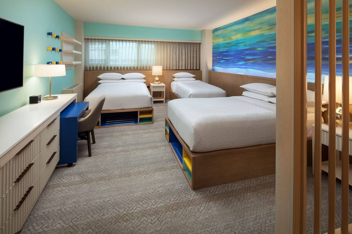 A hotel room with two beds, a desk, a TV, and a painting on the wall.