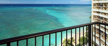 A view from a balcony overlooking turquoise waters with boats, a beach, and a hotel building.