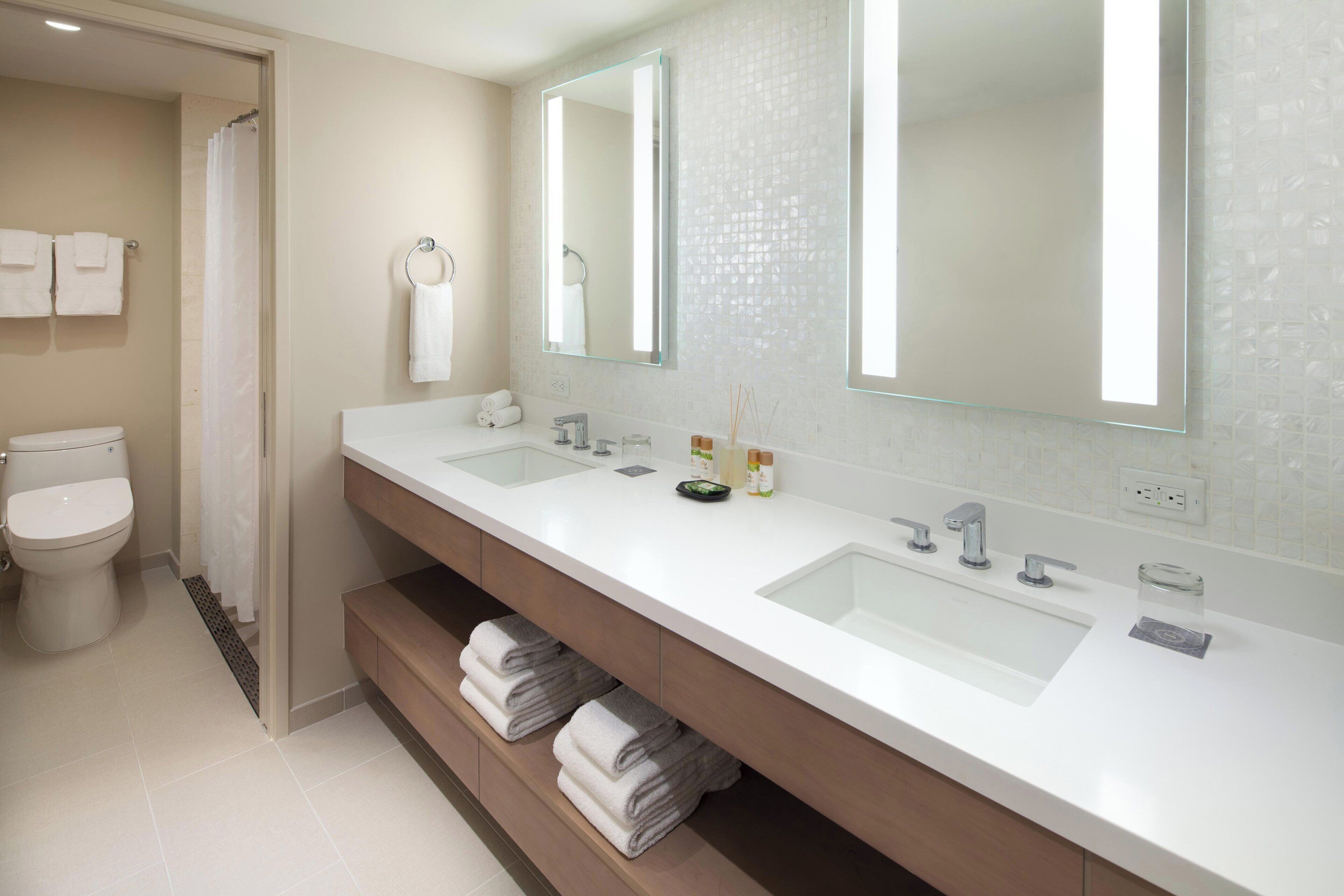A modern bathroom with two sinks, a toilet, and a shower.