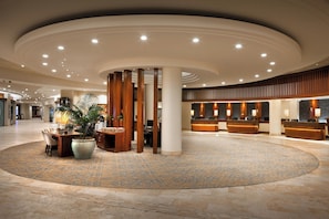 A spacious lobby with a central seating area, a reception desk, and a large decorative plant.