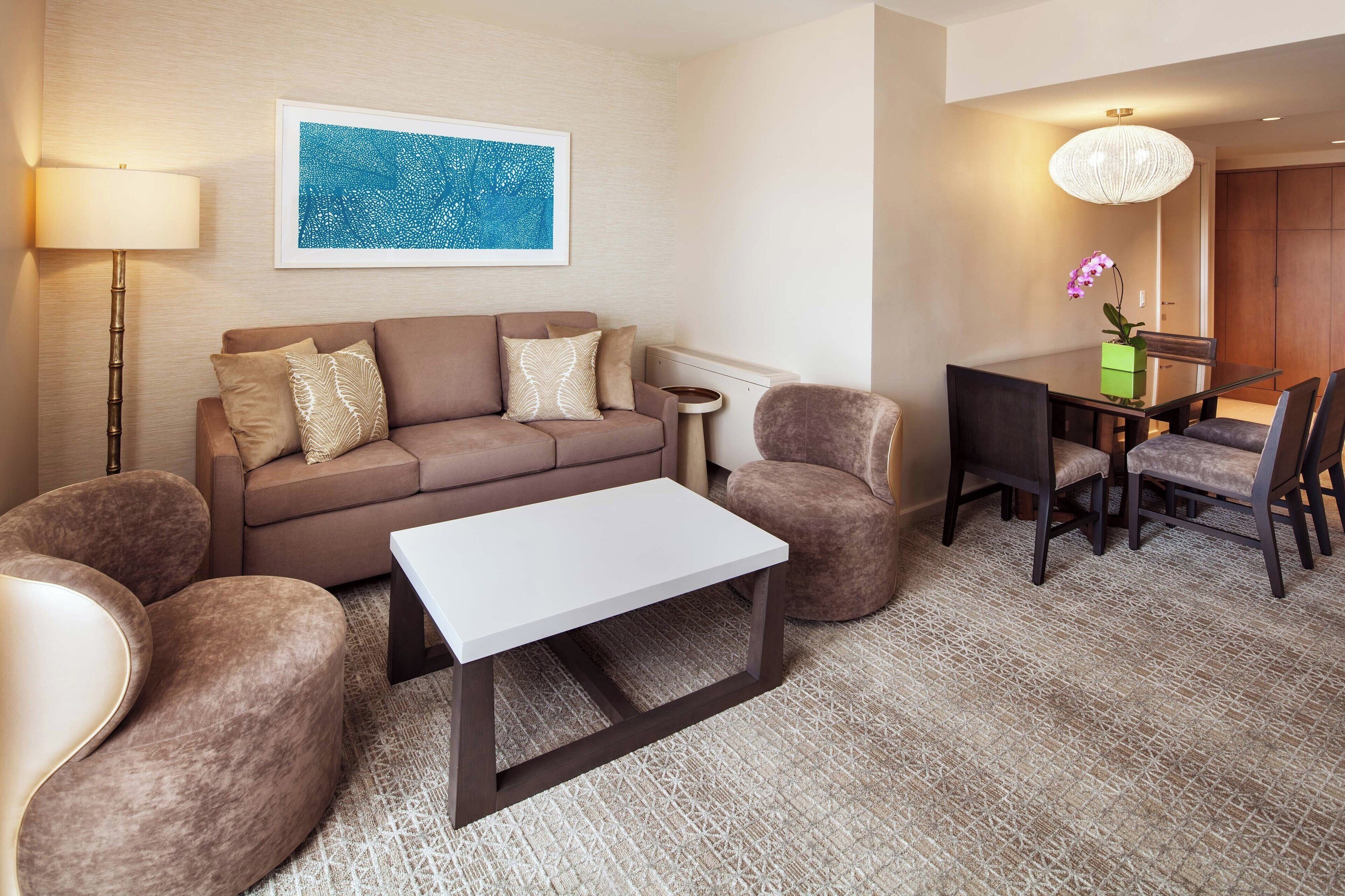 A modern living room with a sofa, armchairs, a coffee table, a dining table with chairs, a floor lamp, and a framed artwork on the wall.