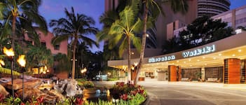 Sheraton Waikiki hotel entrance with a landscaped garden, palm trees, and a water feature.