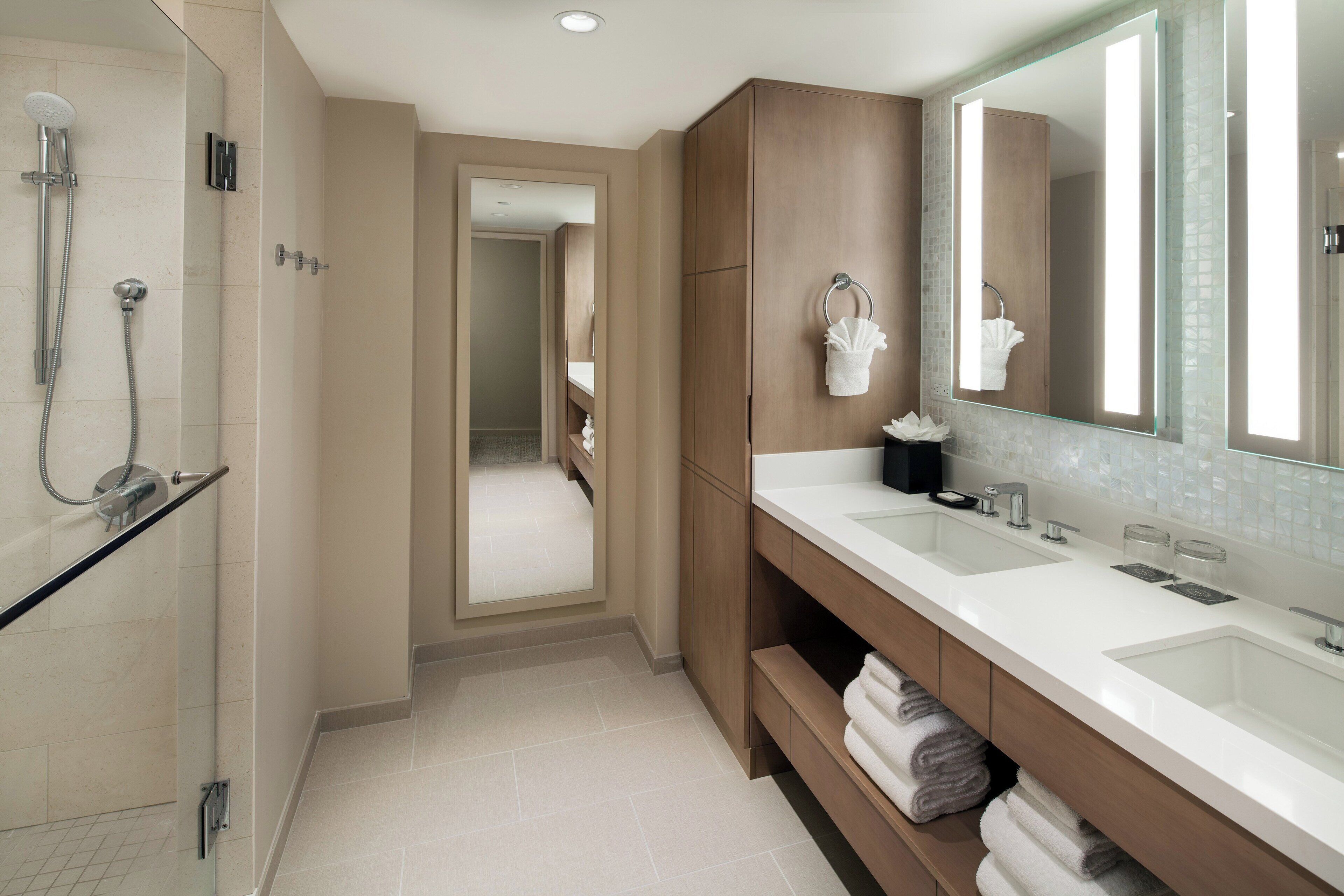 A modern bathroom with a walk-in shower, a large mirror, and a vanity with two sinks.