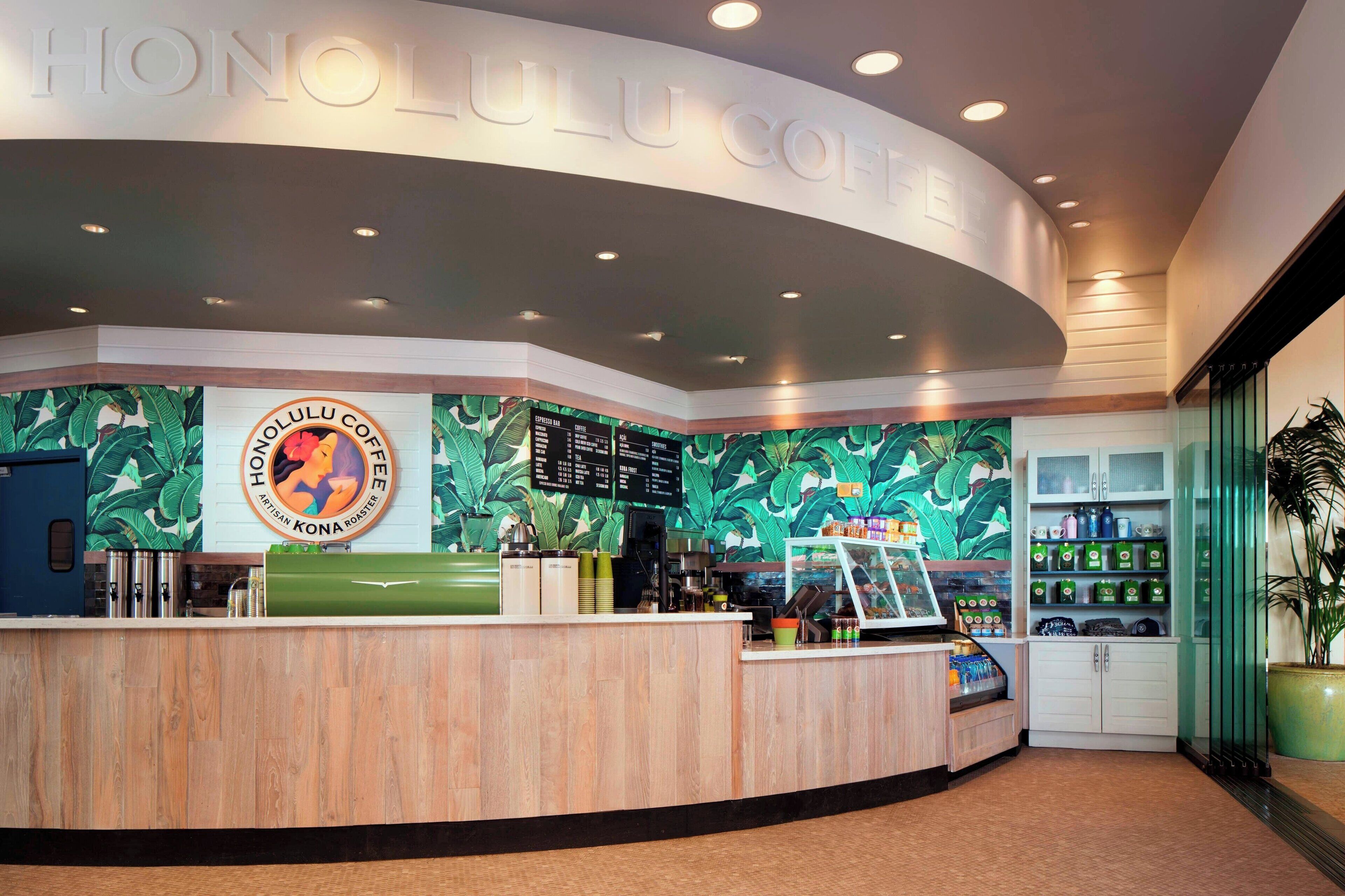A modern coffee shop interior with a wooden counter, a menu board, and a tropical-themed wall.