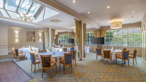 A spacious dining area with tables and chairs, large windows, and a chandelier. - Reigate Manor (Reigate)