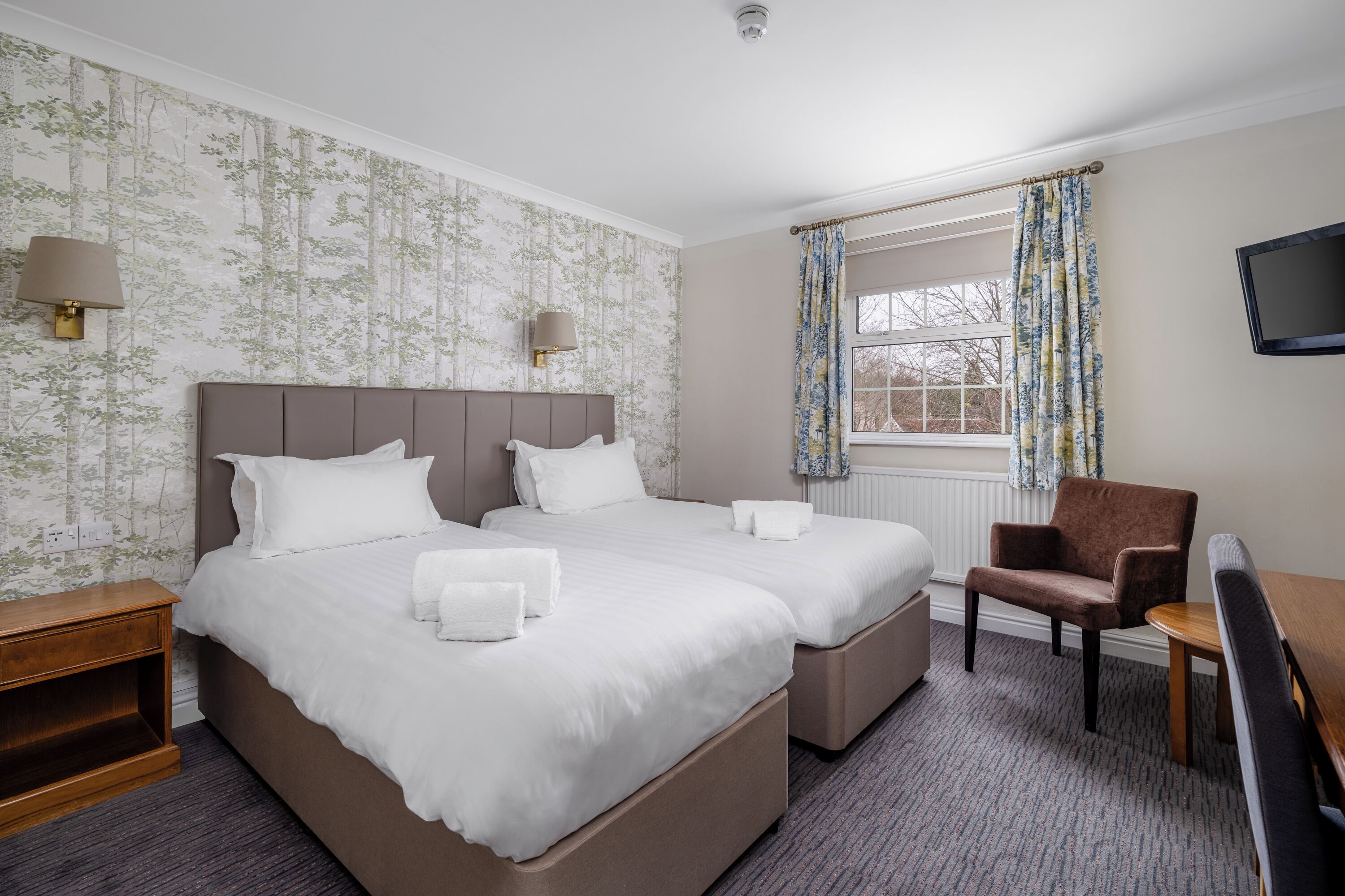 Une chambre d’hôtel avec deux lits, un bureau, une chaise, une télévision et une fenêtre avec des rideaux.