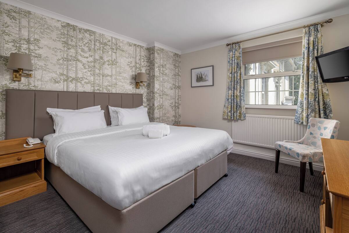 A hotel room with a large bed, bedside lamps, a chair, a TV, and a window with curtains.