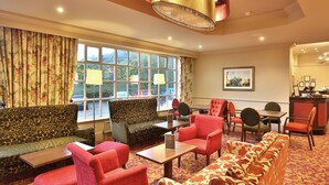 A hotel lobby with a sofa, chairs, a table, and a reception desk. - Reigate Manor (Reigate)