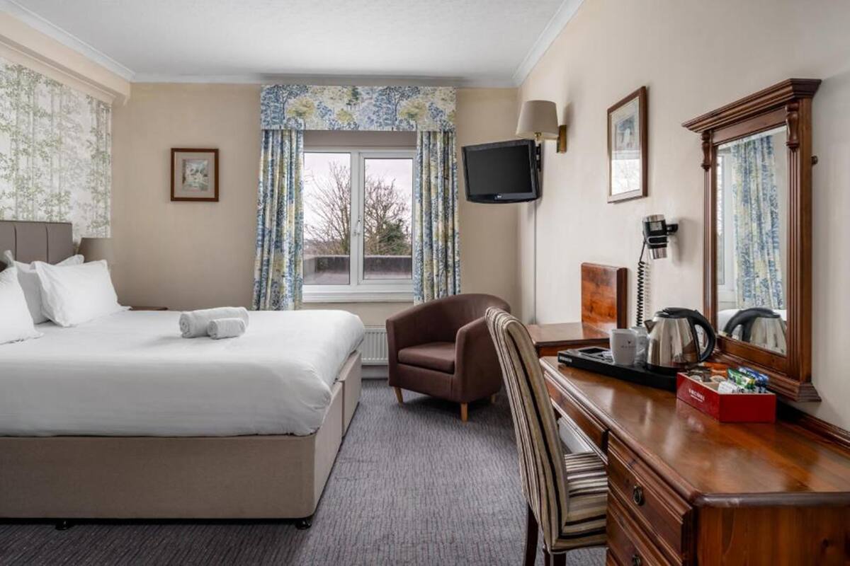 A hotel room with a bed, a desk, a chair, a television, a mirror, and a window with curtains.