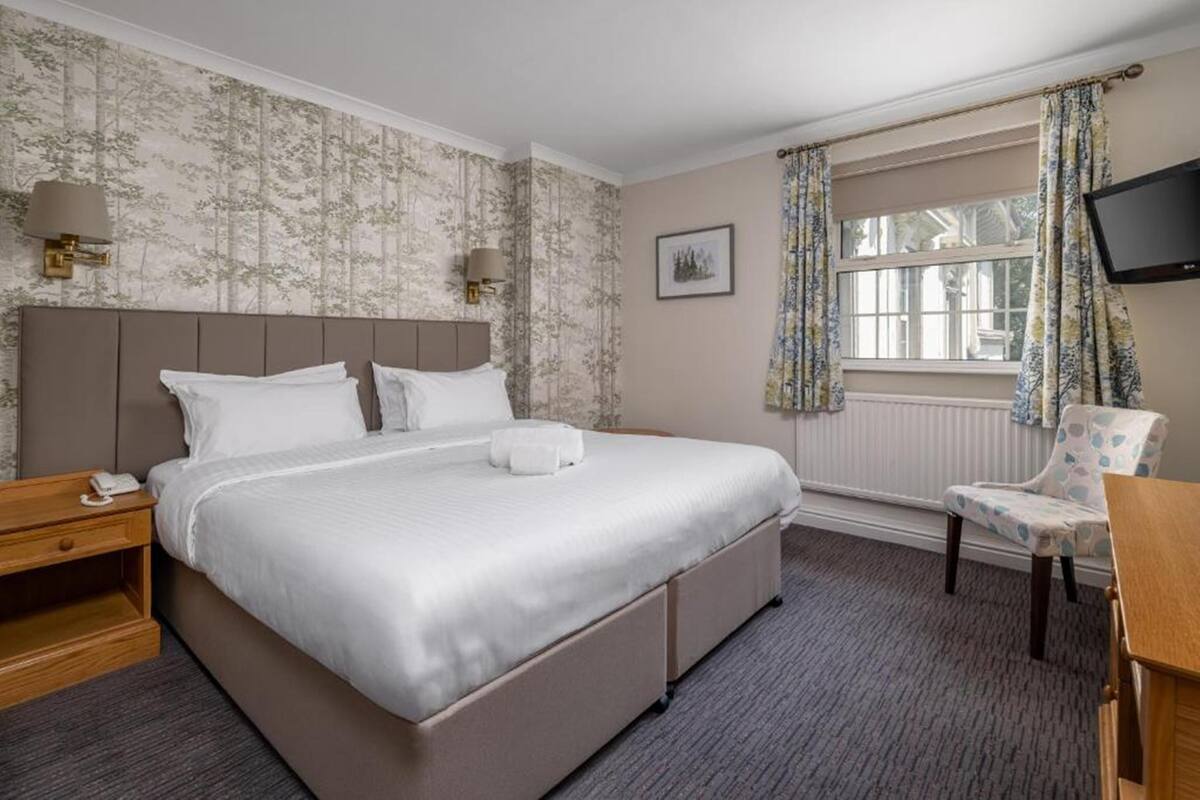 A hotel room with a large bed, bedside lamps, a chair, a TV, and a window with curtains.