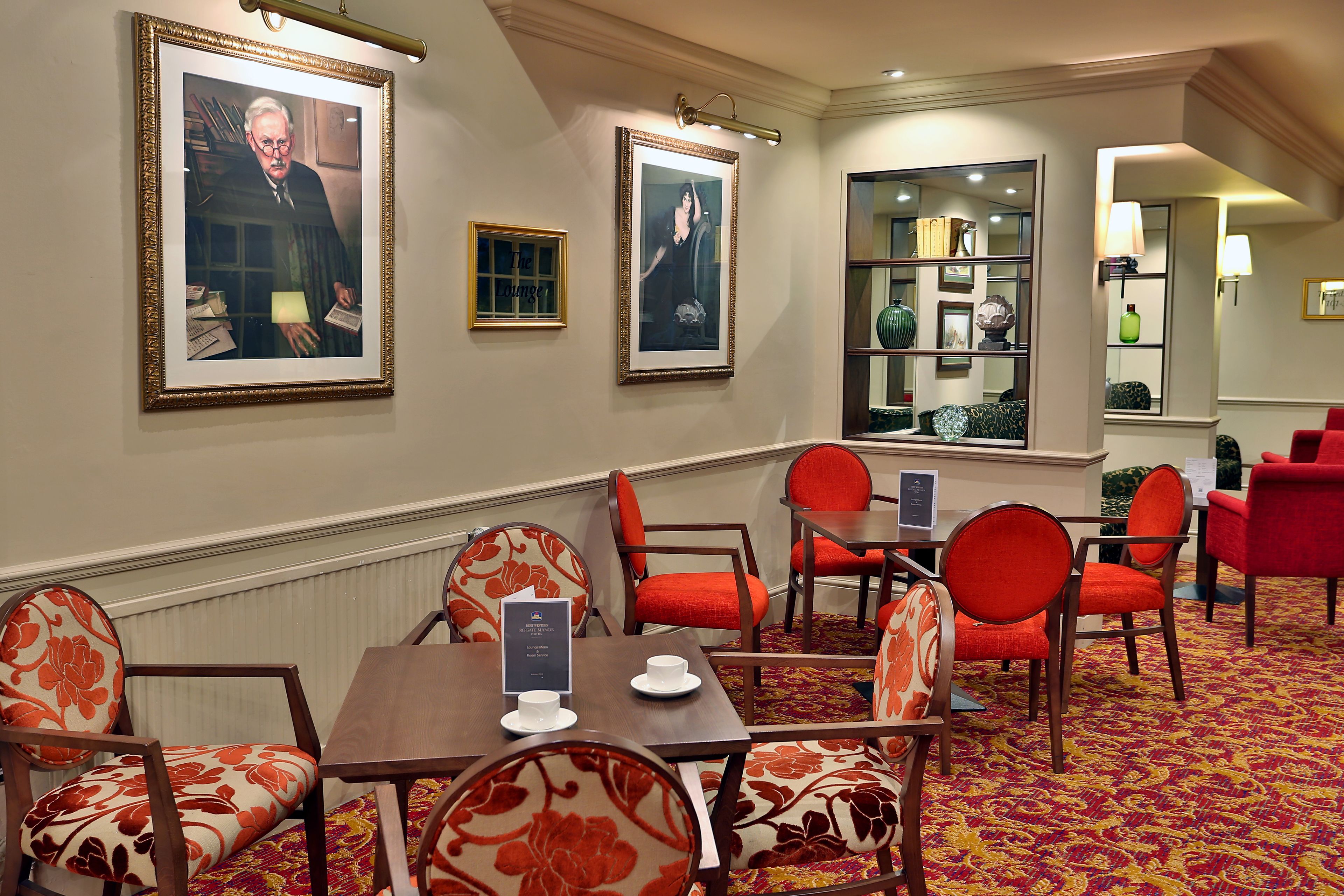 A hotel room with a dining area featuring red and white patterned chairs, a wooden table, and framed artwork on the walls.