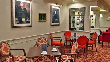 A hotel room with a dining area featuring red and white patterned chairs, a wooden table, and framed artwork on the walls.