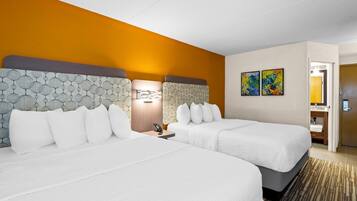 A hotel room with two beds, a nightstand, a lamp, and artwork on the wall.
