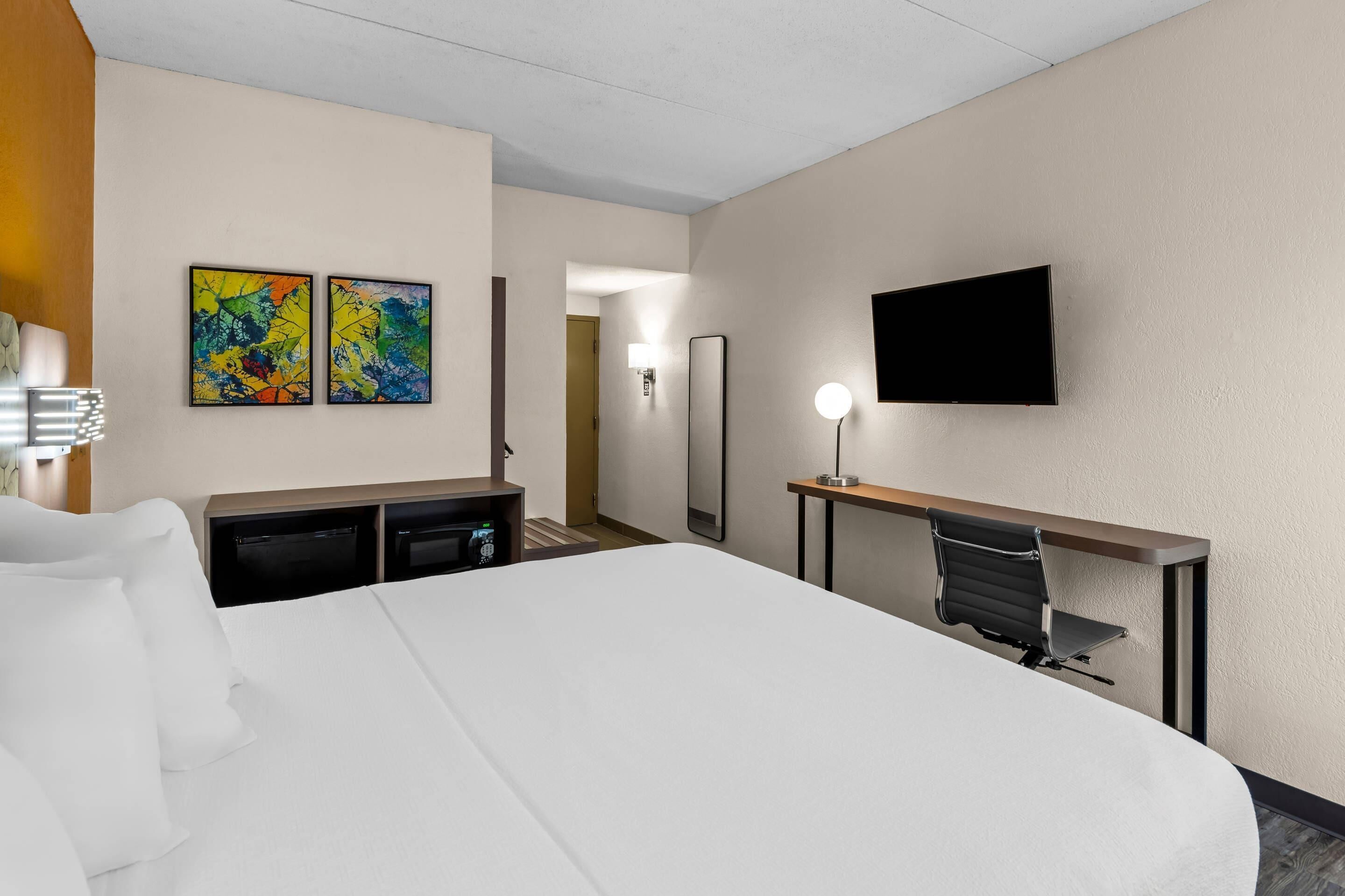 Habitación de hotel con cama, escritorio, silla, televisión y dos cuadros abstractos en la pared.