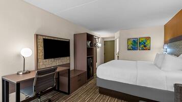 A hotel room with a bed, desk, chair, TV, wardrobe, and artwork on the wall.