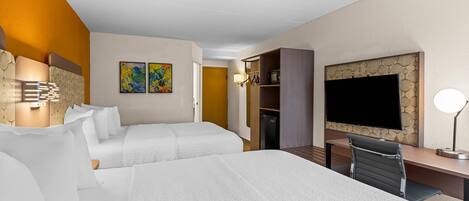 A hotel room with two beds, a desk, a TV, and artwork on the walls.
