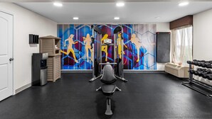 Ett gym med träningsutrustning, en vattenautomat och en färgstark väggmålning.