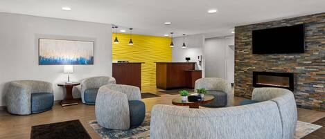A modern living room with a sofa set, a fireplace, a flat-screen TV, and a reception desk.