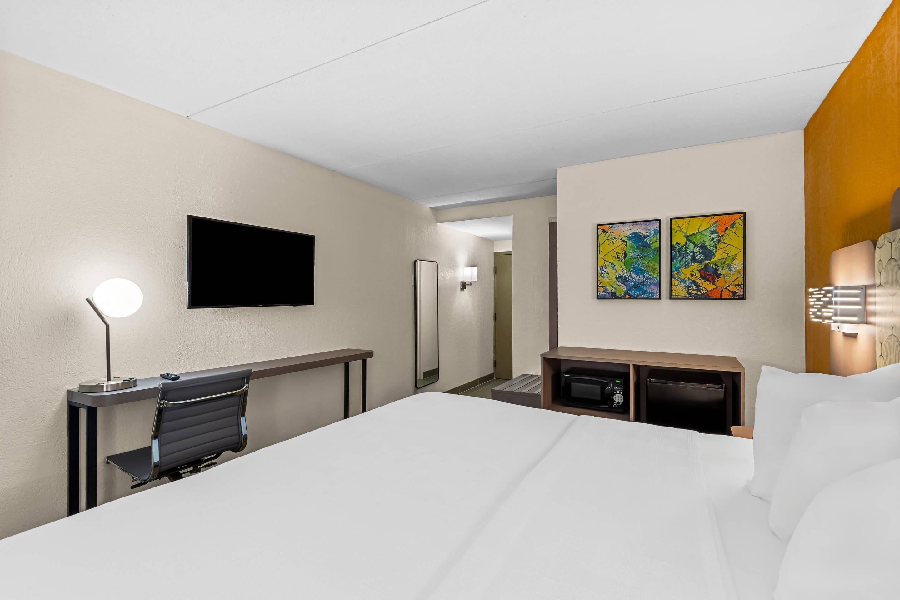 Une chambre d’hôtel équipée d’un lit, d’un bureau, d’une chaise, d’une télévision, d’œuvres d’art et d’un mini-bar.