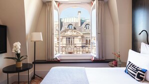 A hotel room with a large bed, a window with curtains, a small table with a lamp, and a potted plant. - Hotel Montalembert (Paris)